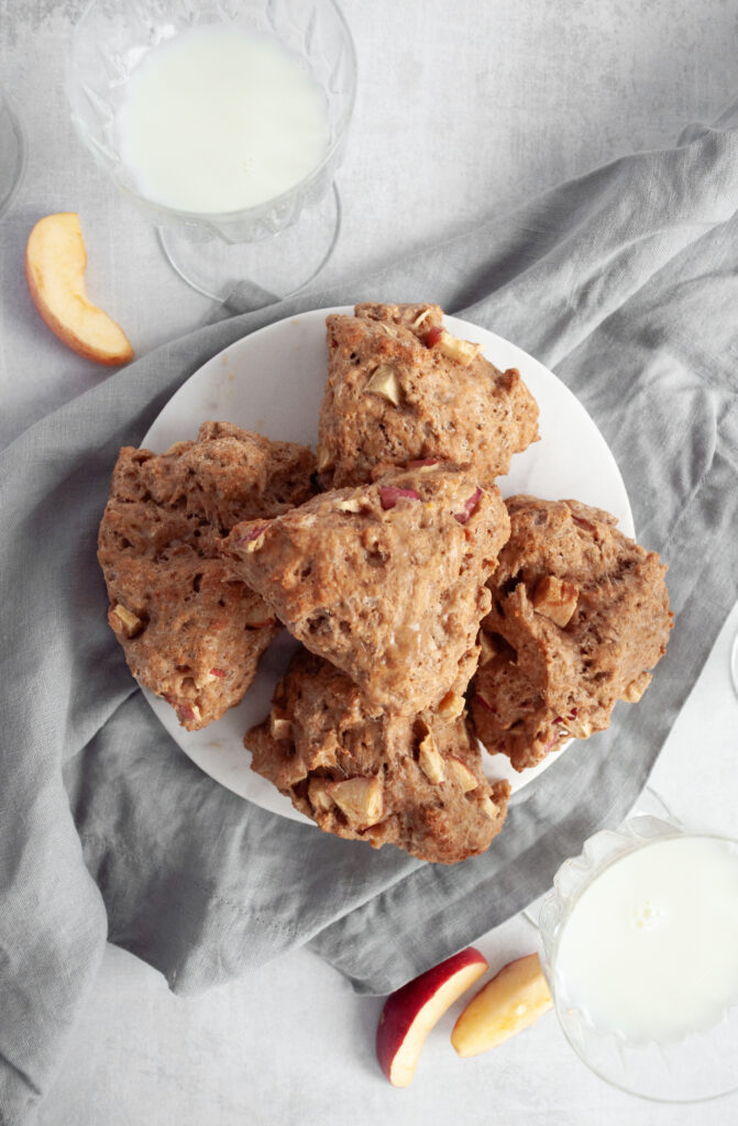 This an image of whole wheat cinnamon apple scones. They are wedge shaped and lying on a plate with a champagne glass full of milk in the background. 